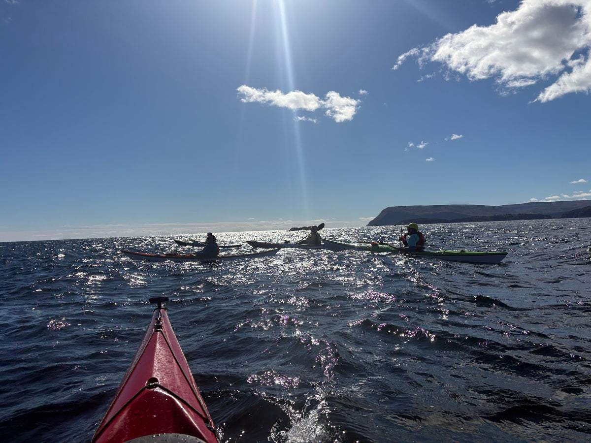 A view from a kayak on the water under a bright sun with clouds, showing other kayakers on the horizon near Cape Smokey.